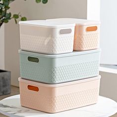 three storage containers stacked on top of each other in front of a window with a potted plant