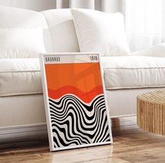 an orange and black poster sitting on top of a wooden floor next to a white couch