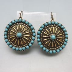 These pretty Mandala shaped earrings are inlaid with pieces of fairly realistic looking faux turquoise set into goldtone metal. They measure  2 inches long (including the wires)  and 1 5/8th inch wide . They have a mandala, wagon wheel design and are light and comfortable on.  They are in MINT condition with no markings. This will arrive in a lovely gift box for easy gift giving or safe storage.  For more pieces of vintage costume jewelry, old silver, bolo ties and vintage accessories, kindly ch Festival Concho Dangle Jewelry, Bohemian Turquoise Beaded Earrings With Brass, Bohemian Turquoise Beaded Earrings In Brass, Bohemian Turquoise Beaded Brass Earrings, Bohemian Turquoise Beaded Earrings, Turquoise Concho Dangle Jewelry, Southwestern Concho Earrings For Festivals, Bohemian Antique Gold Drop Earrings, Turquoise Beaded Brass Jewelry