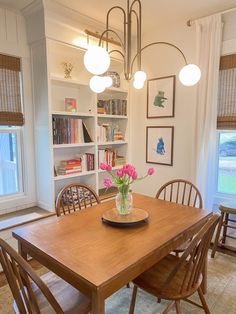 a dining room table with flowers in a vase on top of it and bookshelves