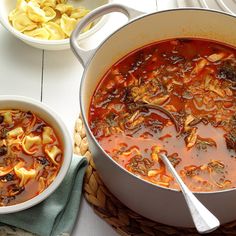 two bowls filled with pasta and meat soup on top of a white table next to a bowl of tortellini shells