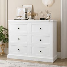 a white dresser sitting in a living room next to a plant