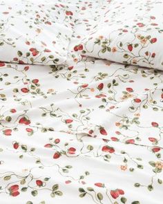 a white bed with red and green flowers on it's comforter, next to a pillow