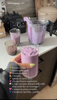 a person holding a glass filled with purple liquid on top of a counter next to other cups