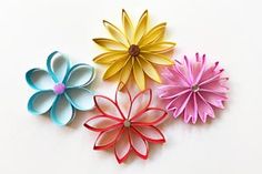 four different colored paper flowers on a white surface