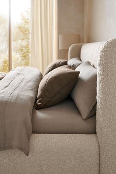 a bed with pillows and blankets on it in front of a window, near a lamp