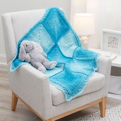 a blue crocheted blanket sitting on top of a chair next to a stuffed animal