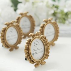 three small gold frames sitting next to each other on a white tablecloth with flowers in the background