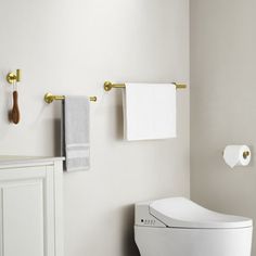 a white toilet sitting in a bathroom next to a sink and towel rack with gold handles