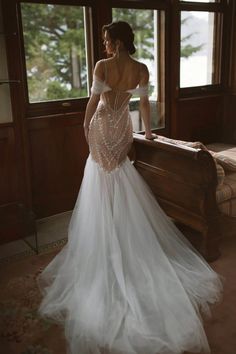 a woman standing in front of a window wearing a wedding dress with an open back