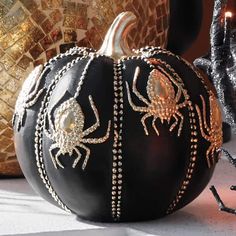 a black pumpkin decorated with gold beading and spider webs sits on a table