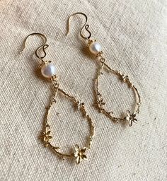 "Enhance your boho chic style with this set of long gold teardrop-shaped flower branch dangly earrings. Featuring large gold-plated brass flower branch charms, these earrings are delicately crafted and exude a sweet charm. The handmade earring hooks, crafted with 10K gold-filled wire, add a touch of elegance. At the top, white freshwater pearls with gold-plated floral bead caps provide a classic and timeless accent. Measuring 2 1/2\" X 7/8\", including the gold-filled wire hooks, these earrings Whimsical Gold Jewelry With Flower Charm, Teardrop Earrings With Flower Charm, Elegant Metal Teardrop Earrings Wire Wrapped, Elegant Metal Teardrop Earrings With Wire Wrapped Detail, Elegant Metal Wire Wrapped Teardrop Earrings, Elegant Teardrop Earrings With Flower Charm, Elegant Gold Wire Wrapped Teardrop Earrings, Whimsical Gold Wire Wrapped Earrings, Gold Whimsical Flower-shaped Earrings