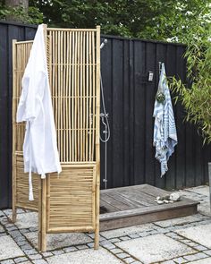 an outdoor shower is next to a wooden bench with towels hanging on the back wall