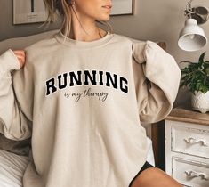 "Embrace the therapeutic rhythm of the run with our \"Running Is My Therapy\" sweatshirt! ot just for the track or trail, this sweatshirt is versatile. Throw it on after a run, or make it your comfy go-to for chilly days. Running is a lifestyle, and now your wardrobe reflects it. HOW TO ORDER: 1. Choose size/color options 2. Select the quantity 3. Click \"Add to Cart\" 4. Proceed to payment Sweatshirt Features: - Premium blend Organic Cotton  - Relaxed fit/ Unisex - Available in sizes S - 5XL Care Instructions: To keep your sweatshirt looking its best, follow these care instructions: - Machine wash cold with like colors. - Use only non-chlorine bleach when needed. - Tumble dry low or hang to dry for best results. - Iron on low heat if necessary, avoiding the printed area. SIZING: While the Sporty Fleece Sweatshirt For Gym, Sportswear Hoodie For Running And Sports Season, White Letter Print Sweatshirt For Gym, White Letter Print Sweatshirt For The Gym, Team Spirit Hoodie Sweatshirt For Sports, Workout Sweatshirt With Letter Print For Sports Season, Letter Print Sweatshirt For Sports Season Workout, Sporty Sweat-resistant Running Hoodie, Sporty Stretch Hoodie With Graphic Print