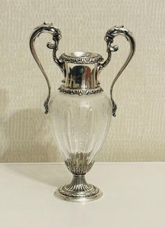 an ornate silver vase sitting on top of a white table next to a beige wall