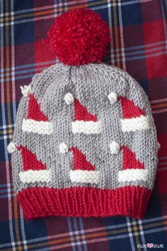 a knitted hat sitting on top of a plaid blanket with a red pom - pom