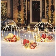 three decorative christmas balls sitting in front of a house with lights on the outside and inside