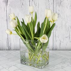 white tulips are in a clear vase on a marble countertop with water