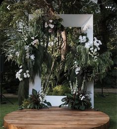 a wooden table topped with white flowers and greenery next to a mirror in the grass