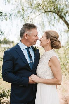 a man and woman are standing together in front of some trees, one is kissing the other