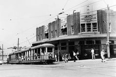 an old black and white photo of people walking on the sidewalk in front of a trolley car