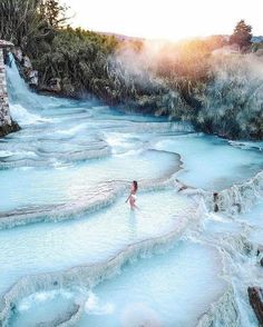 a woman is wading in the water near a waterfall