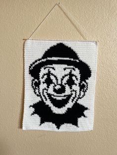 a crocheted image of a smiling clown hanging on a wall