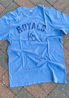 a blue kansas royals t - shirt laying on the ground in front of a brick sidewalk