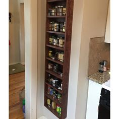 a tall wooden spice rack in the corner of a living room next to a kitchen