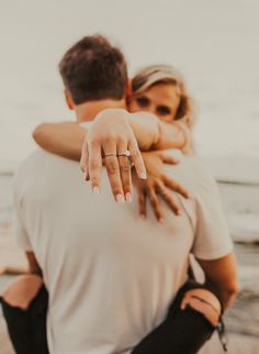 a man and woman hugging each other on the beach with their hands wrapped around them