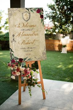 a welcome sign with flowers on it in front of a grassy area at a wedding