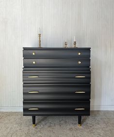 a black dresser with brass handles and knobs on it's sides, against a white wall