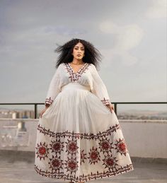 a woman standing on top of a roof wearing a white dress with red trims