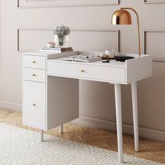 a white desk with two drawers and a gold lamp on the table next to it