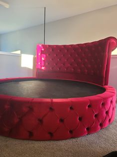 a round bed with red velvet upholstered headboard and footrests in a living room