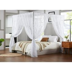 a white canopy bed sitting on top of a hard wood floor next to a window