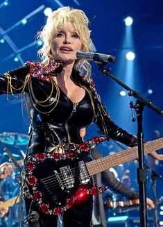 a woman in black outfit holding a guitar on stage