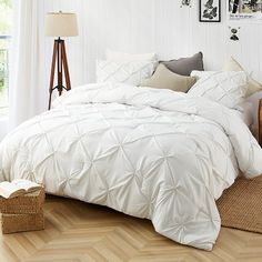 a bed with white comforter and pillows in a room next to a lamp on a wooden floor