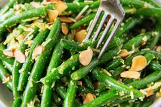 a bowl filled with green beans and nuts next to a fork in the side dish