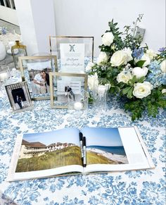 an open book sitting on top of a table next to pictures and flowers in vases