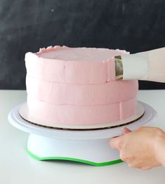 a person is decorating a pink cake with icing on the top and bottom