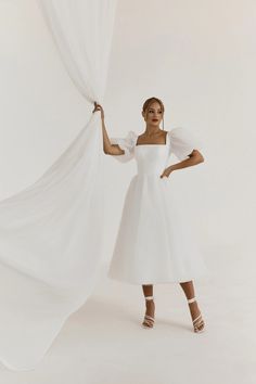 a woman in a white dress is holding curtains