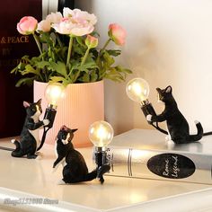 three black cats sitting on top of a table next to a book and light bulb