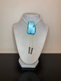 Turquoise faux stone, white braided leather adjustable bolo tie. Stone sizes and shapes vary, they will not be shaped exactly like the one pictured. Southwestern Bolo Tie With Sliding Knot, Southwestern Lariat Turquoise Necklace, Southwestern Adjustable Lariat Turquoise Necklace, Adjustable Southwestern Turquoise Lariat Necklace, Southwestern Adjustable Turquoise Lariat Necklace, Artisan Turquoise Adjustable Lariat Necklace, Artisan Turquoise Lariat Necklace Adjustable, Artisan Adjustable Turquoise Lariat Necklace, Artisan Bolo Ties With Sliding Knot As Gift