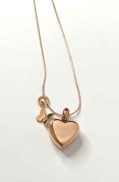 a gold heart necklace with two hearts hanging from it's sides on a white surface