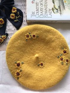 a yellow hat with sunflowers on it next to a book and some hair clips