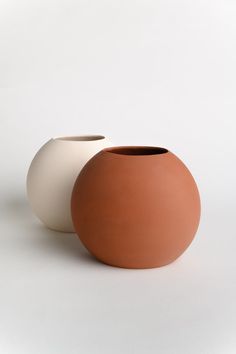 two clay vases sitting side by side on a white surface, one with an oval shape and the other without