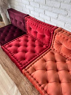 four different colored cushions sitting next to each other on the floor in front of a white brick wall