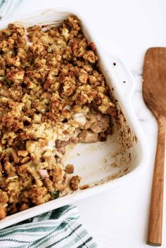 a casserole dish filled with stuffing next to a wooden spoon