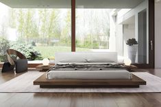 a modern bedroom with wood flooring and white bed in front of large window overlooking trees